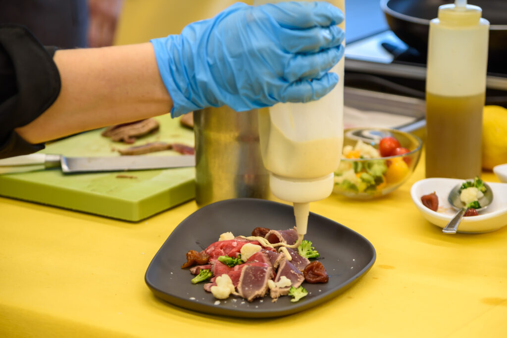 Los chefs echando salsa a la ensalada italiana hecha a base de lomo de atún